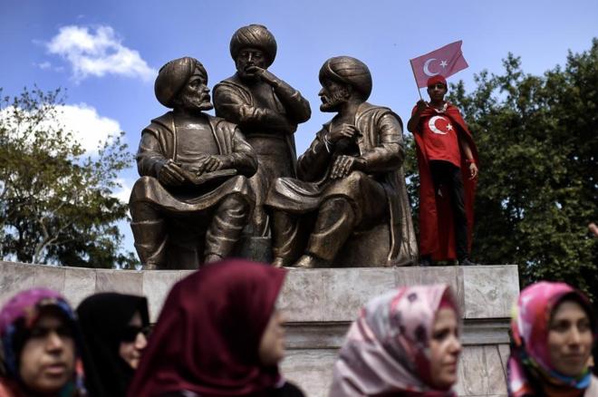 Un niño con una bandera turca junto a la estatua del sultán Mehmed II