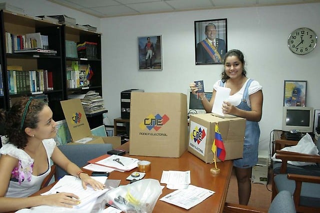 La mesa electoral y una ciudadana votante con su boleta electoral y la Constitución en sus manos