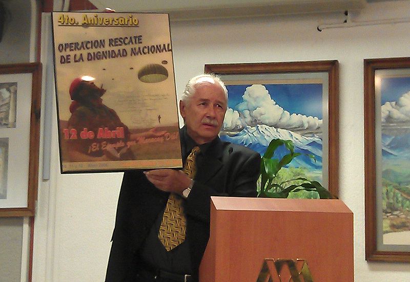 Heinz Dieterich durante su discurso en solidaridad con la Revolución Bolivariana en la Universidad Autónoma Metropolitana de México (UAM) en 2013, muestra un afiche del General Raúl Baduel conmemorando el 4to aniversario de la operación rescate de la dignidad nacional de abril 2002.