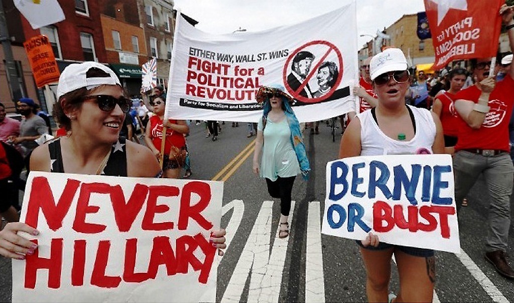 "Sanderistas" militantes del Partido Socialista Liberación, marchando previo a la convención portando una pancarta que se lee: "luchemos por una revolución política"..En primer plano se lee: "nunca Hillary"