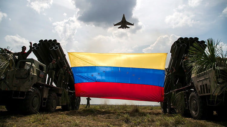 Un avión de combate Sukhoi Su-30MKV de fabricación rusa de la Fuerza Aérea venezolana vuela sobre una bandera venezolana atada a lanzadores de misiles durante el ejercicio militar "Escudo Soberano 2015", en San Carlos del Meta, estado Apure. Abril, 2015.