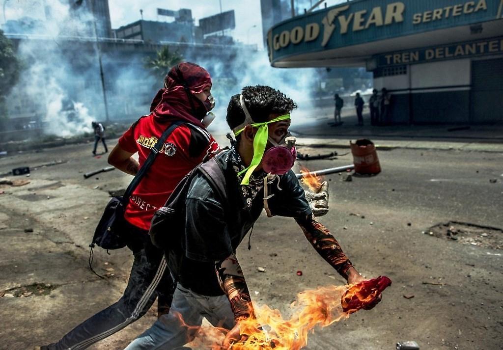 Dos jóvenes protestando "pacíficamente" en Caracas, casualmente la foto tiene como escenario de fondo un concesionario de una marca de cauchos estadounidense.