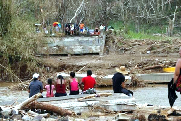 Varias personas permanecen sentadas en ambos lados de los restos de un puente destruido en la isla.