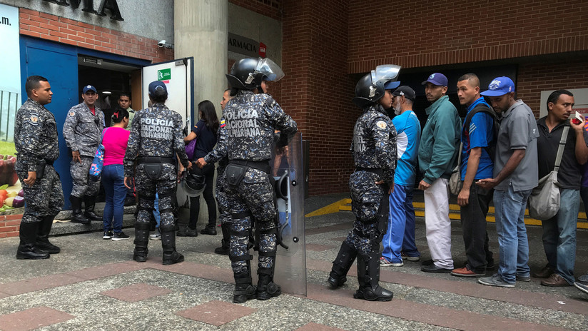 Policías custodian una fila de gente que compra azúcar a las afueras de un supermercado en Caracas.