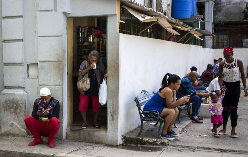 Gente navega en internet con sus teléfonos celulares cerca de una plaza en La Habana