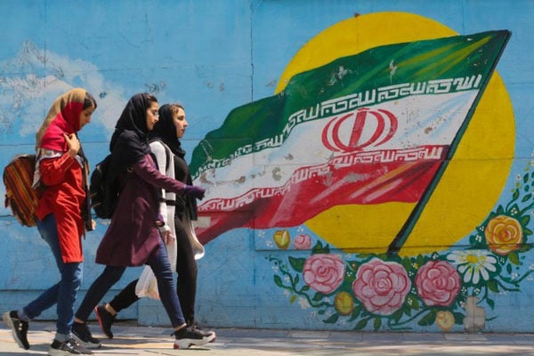 Un grupo de chicas jóvenes caminan delante de un mural con la bandera iraní en Teherán