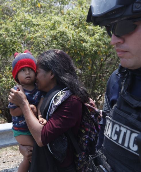 Una mujer migrante centroamericana y su hijo caminan con un agente de la Policía Federal de México mientras son detenidos en la carretera a Pijijiapan, México.