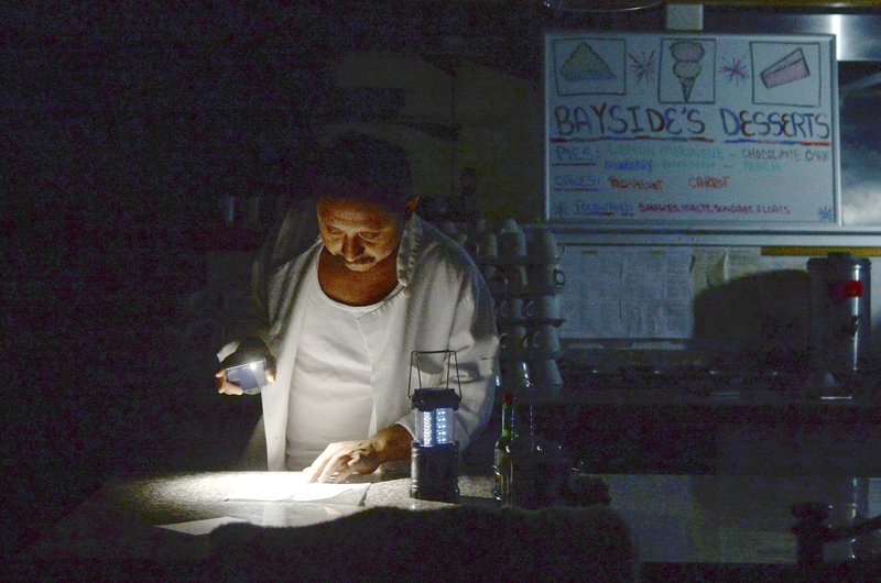 Un afectado por los apagones, utiliza una linterna LED y luz de su teléfono en su restaurante en Sausalito, California