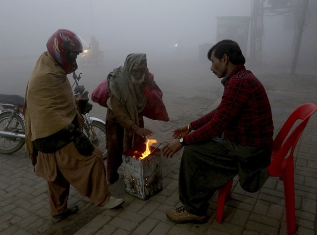 Personas se reúnen en torno a un pequeño fuego durante una mañana fría en Lahore, Pakistán