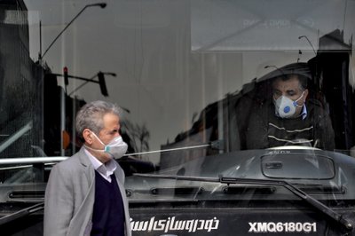 El conductor de un autobús de transporte público y un peatón utilizan cubrebocas para evitar un contagio del coronavirus en el centro de Teherán, Irán