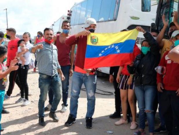 Un grupo de venezolanos, varados en Bogotá, muestra una bandera junto a los buses que fueron rentados para regresar a su país.