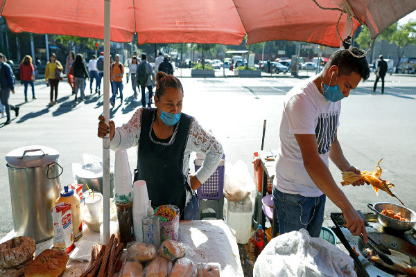 Trabajadores ambulantes usan mascarillas protectoras mientras venden tamales, sándwiches y pasteles en un puesto callejero en la Ciudad de México, el miércoles 25 de marzo de 2020.