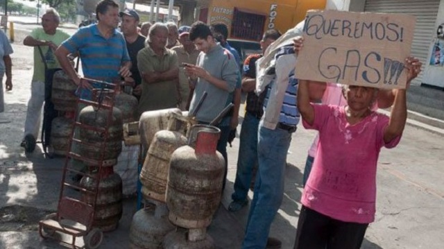 Vecina exhibe en cola para adquirir gas doméstico un cartel pidiendo el combustible imprescindible para cocinar en los hogares