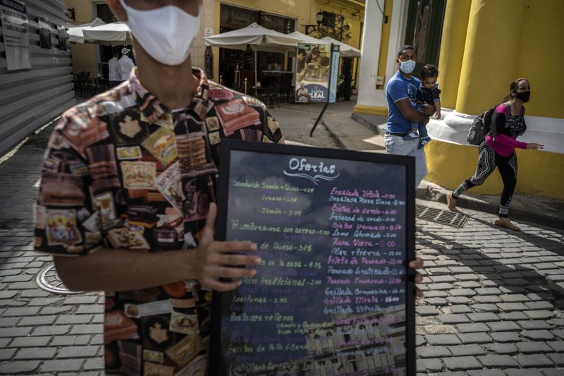 Mesonero con su mascarilla exhibe ofertas de restaurant en La Habana