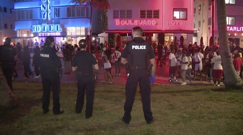 Policías vigilando el sábado 20 de marzo, mientras una muchedumbre recorre una calle de South Beach, Miami