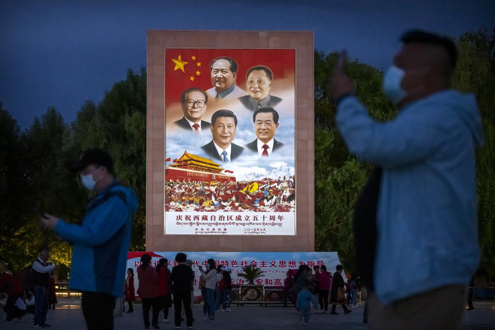 Visitantes se toman fotos bajo un gran cartel con imágenes de Mao Zedong, Deng Xiaoping, Hu Jintao, Xi Jinping y Jiang Zemin, al pie del Palacio Potala de Lhasa, capital de la Región Autónoma del Tíbet