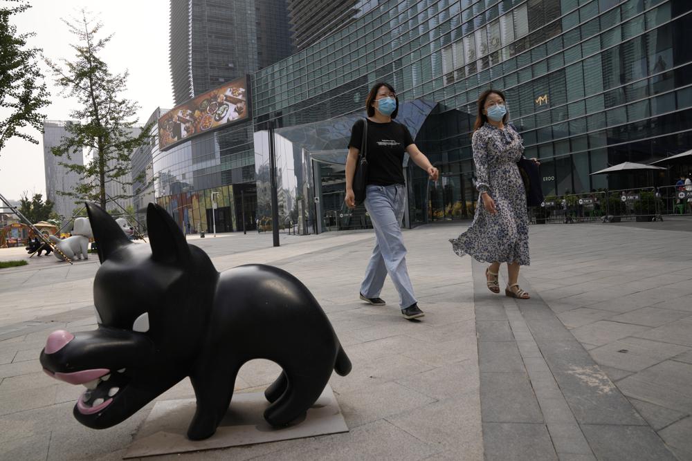 Mujeres que llevan mascarillas debido al coronavirus pasan cerca de la escultura de un perro en Beijing, China