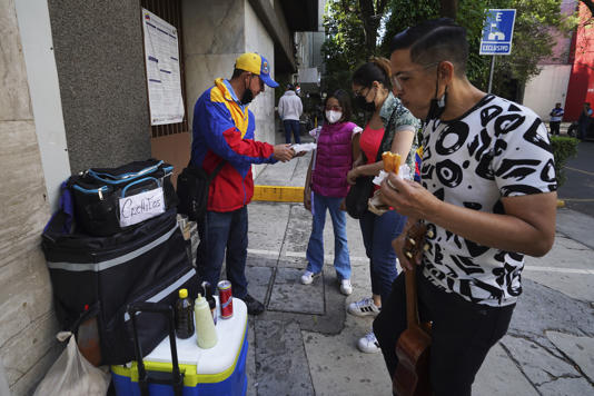 Venezolanos que viven en Ciudad de México le compran empanadas y otros productos de su tierra al vendedor callejero Nelson Banda frente a la embajada de Venezuela en la capital mexicana
