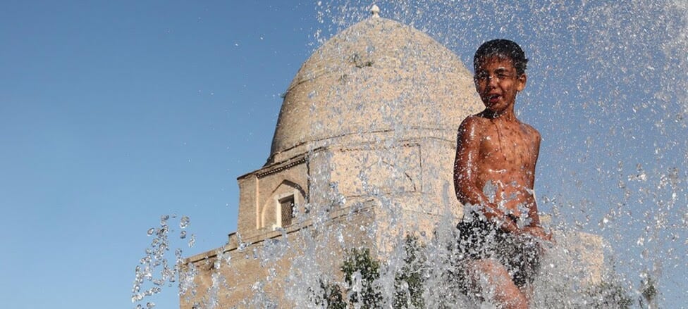 Un niño se refugia del calor en una fuente de la ciudad de Samarcanda, en Uzbekistán. Las altas temperaturas castigan a todo el hemisferio norte, acompañadas de lluvias e inundaciones devastadoras, en una situación descrita como "nueva normalidad" y que requiere intensificar la lucha contra el cambio climático